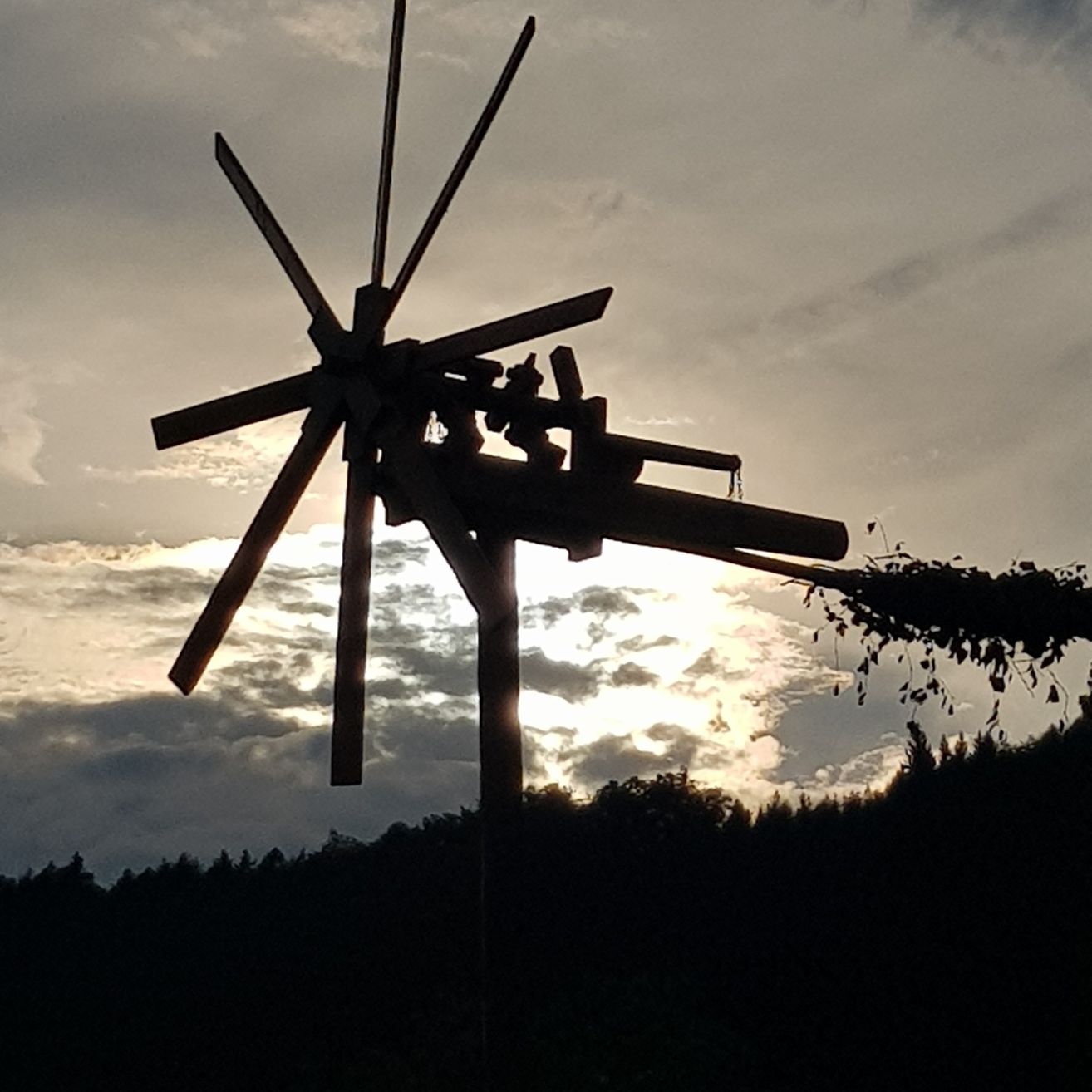 Die Silhouette eines Windrads mit Blättern am unteren Ende vor einem bewölkten Himmel.