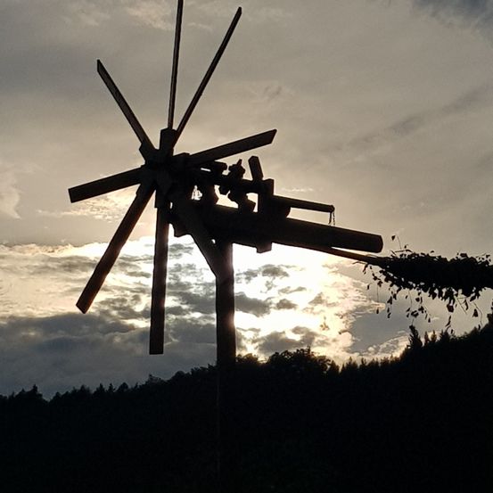 Die Silhouette eines Windrads mit Blättern am unteren Ende vor einem bewölkten Himmel.
