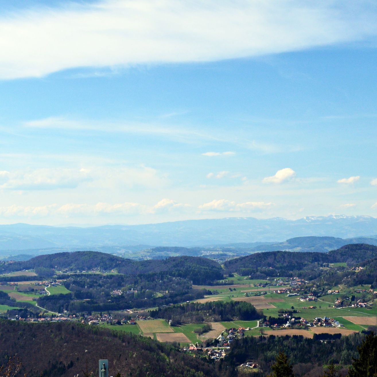 Ein Panoramablick auf eine Berglandschaft mit einem Tal, einigen Gebäuden und einem klaren blauen Himmel mit Wolken.