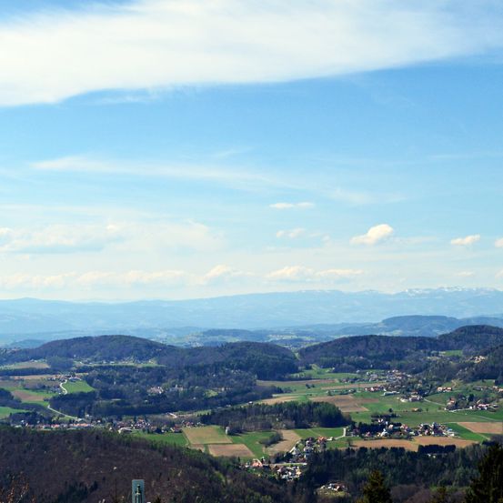 Ein Panoramablick auf eine Berglandschaft mit einem Tal, einigen Gebäuden und einem klaren blauen Himmel mit Wolken.
