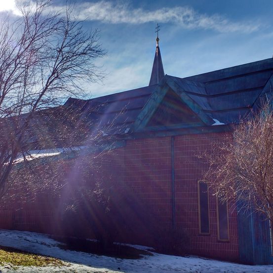 Eine Kirche mit einem Kirchturm und roten Backsteinmauern. Sie ist von Schnee umgeben, und Sonnenlicht scheint auf das Gebäude und die Bäume.