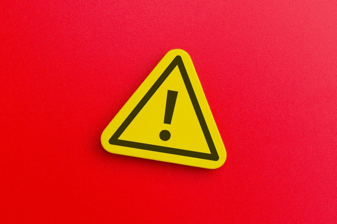 Ein gelbes dreieckiges Warnzeichen mit einem schwarzen Ausrufezeichen in der Mitte, das auf einem roten Hintergrund platziert ist.