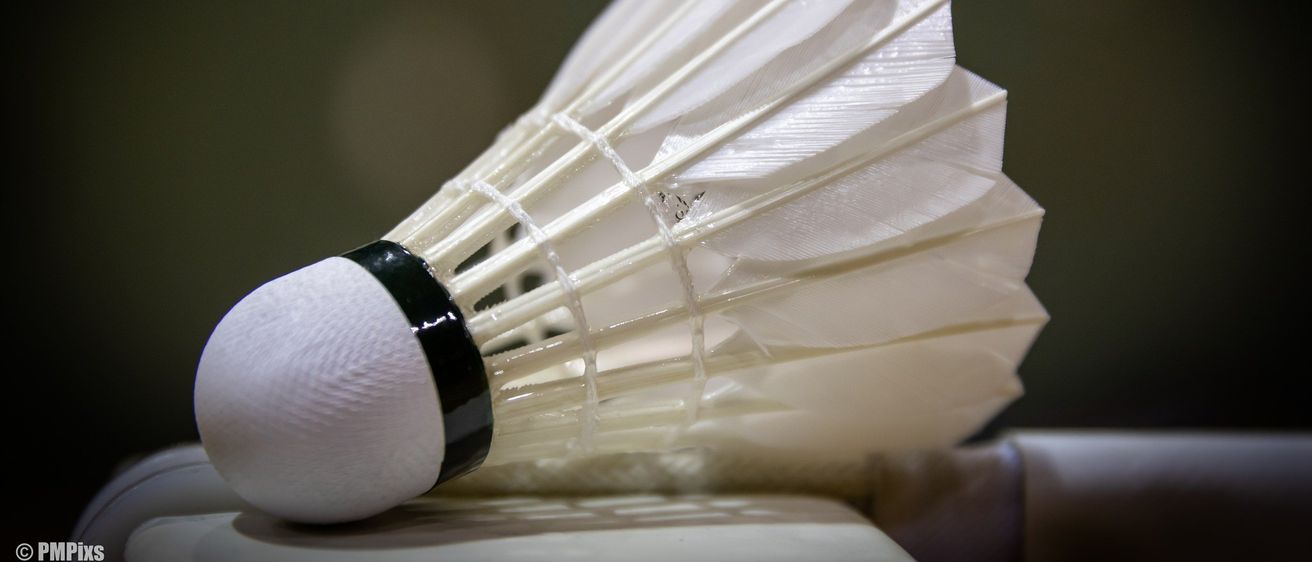 Eine Nahaufnahme eines Badminton-Federballs mit weißen Federn und einem schwarzen Band um die Basis, auf einer weißen Oberfläche platziert.