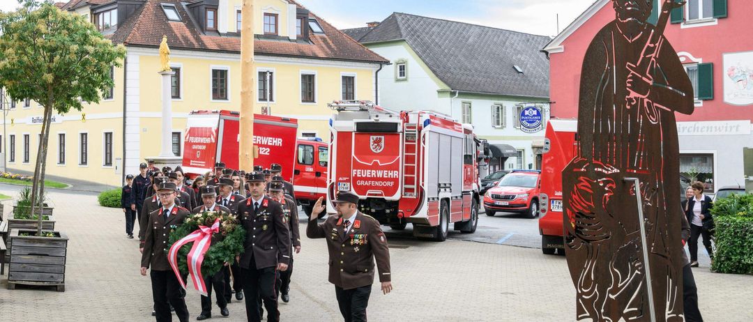 Ein Militäraufmarsch mit Feuerwehrwagen und einer Girlande vor einem Gebäude.