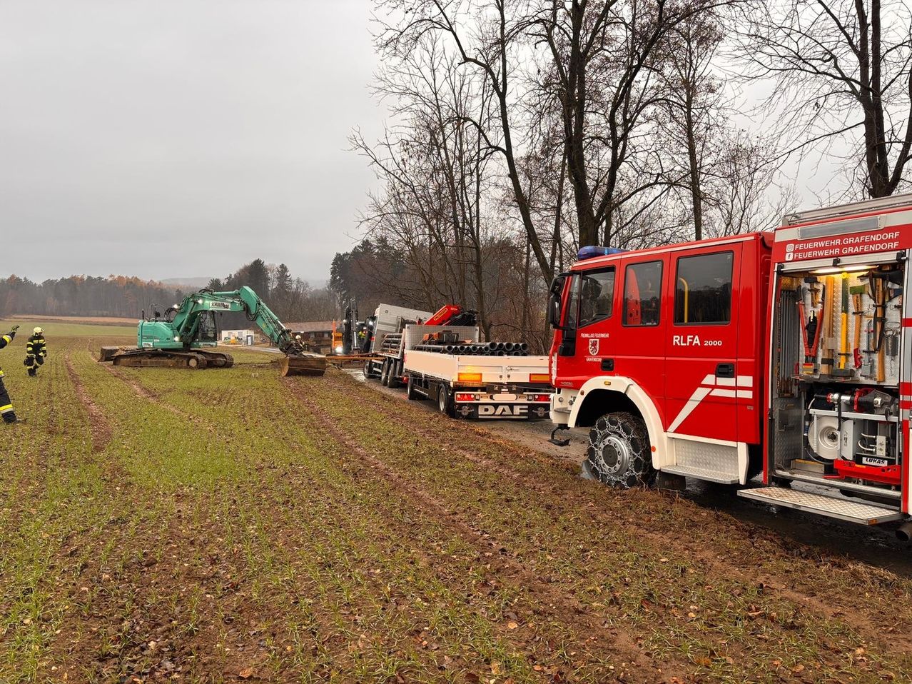 Ein roter Feuerwehrwagen steht auf einem Feldweg, im Hintergrund befindet sich ein Baufahrzeug.