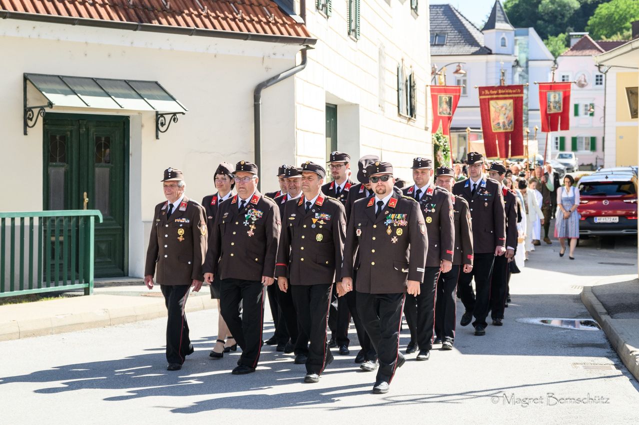 A group of men in military uniforms are marching down the street. They are wearing medals and have red stripes on their pants.