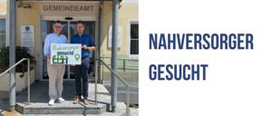 Zwei Männer stehen auf Stufen und halten ein Schild mit der Aufschrift 'nachversorger gesucht'. Sie stehen vor einem Gebäude.