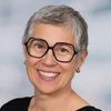 Eine Frau mit grauen Haaren, die eine Brille und ein schwarzes Shirt trägt, lächelt in die Kamera.