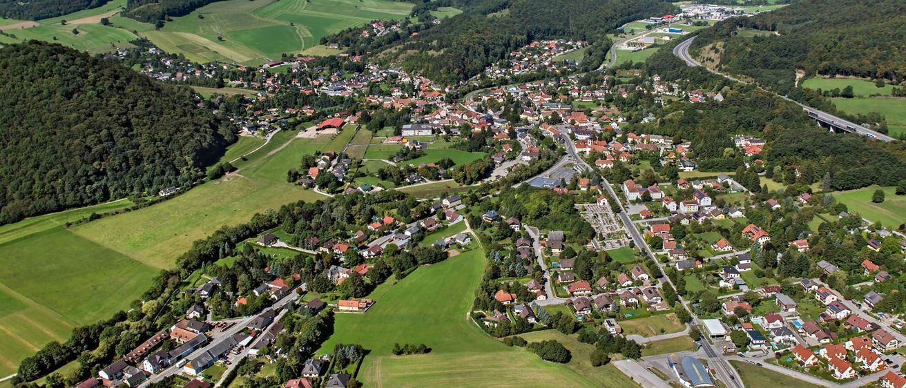 Eine Luftaufnahme einer Stadt, umgeben von üppigen grünen Feldern und Bergen unter einem klaren blauen Himmel.