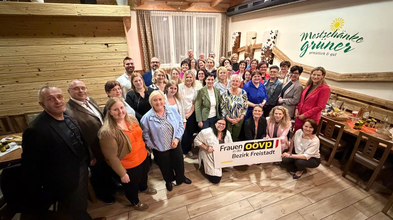 Eine Gruppe von Menschen posiert für ein Foto in einem Raum. Eine Person in der Mitte hält ein Banner mit dem Text Frauen oovp in der Bezirk Freistadt.
