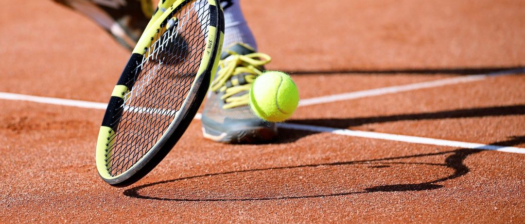 Ein Tennisspieler steht auf einem Sandplatz und ist bereit, einen Tennisball mit einem gelben und schwarzen Schläger zu schlagen.