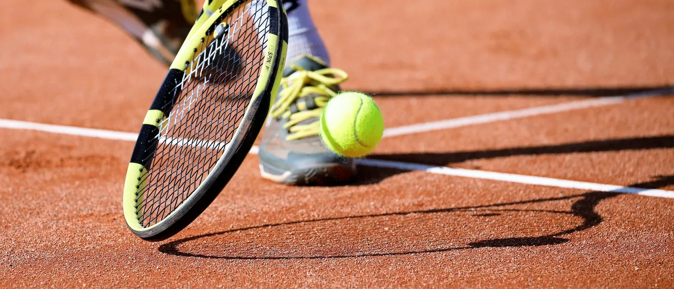 Ein Tennisspieler steht auf einem Sandplatz und ist bereit, einen Tennisball mit einem gelben und schwarzen Schläger zu schlagen.