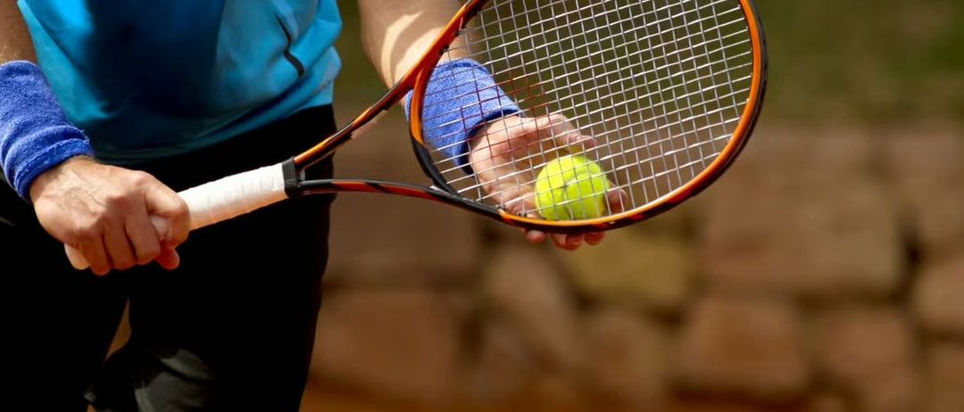 Eine Person hält einen Tennisball und Schläger in der Hand, bereit zum Spielen auf einem Tennisplatz.
