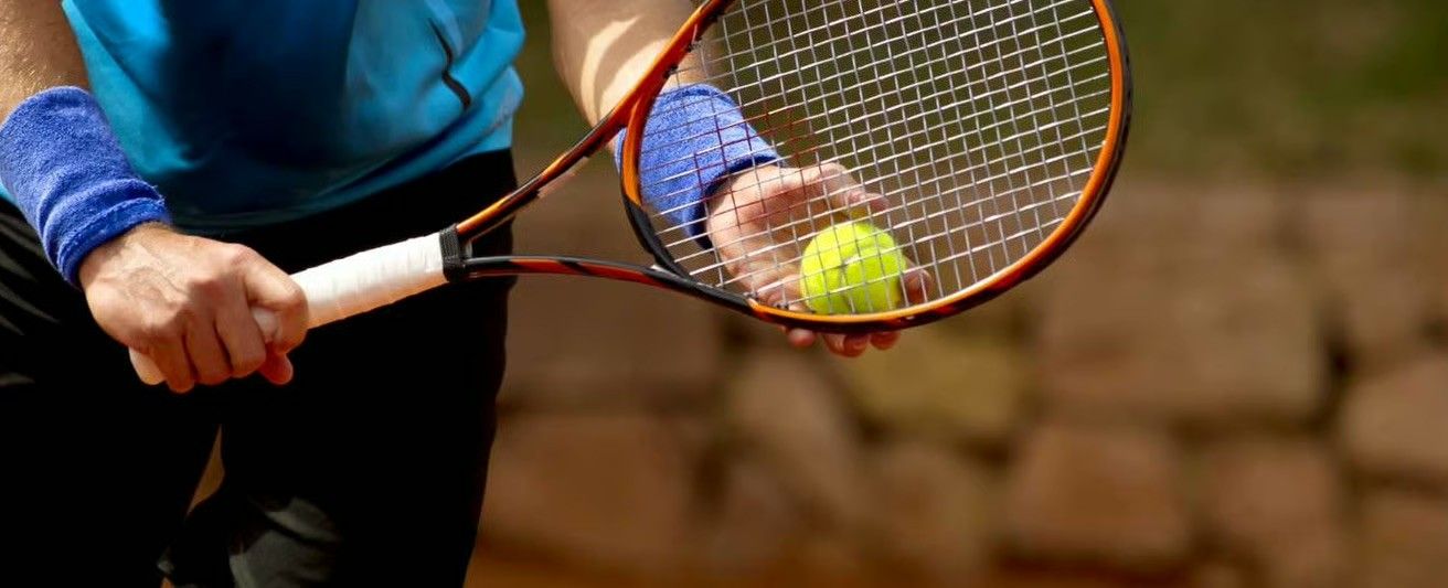 Eine Person hält einen Tennisball und Schläger in der Hand, bereit zum Spielen auf einem Tennisplatz.