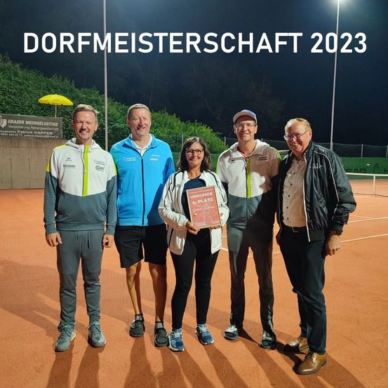 Fünf Personen stehen auf einem Tennisplatz und halten eine Plakette. Die Frau in der Mitte trägt eine Brille und eine weiße Jacke. Der Text 'DORFMEISTERSCHAFT 2023' ist oben.