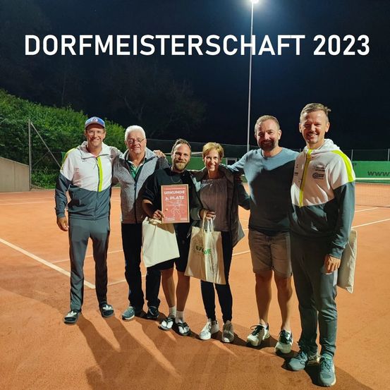 Eine Gruppe von fünf Personen posiert nachts auf einem Tennisplatz. Eine Frau hält eine rote Plakette. Die Worte 'Dorfmeisterschaft 2023' sind oben angezeigt.