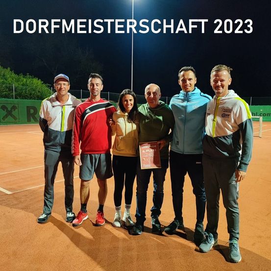 Fünf Personen stehen auf einem Tennisplatz und posieren für ein Foto. Sie tragen alle Turnschuhe. Der Mann in der Mitte hält ein Zertifikat. Der Hintergrund ist ein Nachthimmel mit Bäumen.