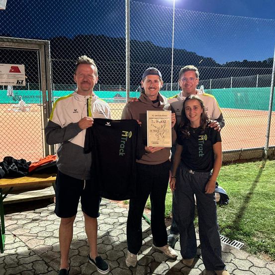 Vier Personen posieren auf einem Tennisplatz für ein Foto, einer hält ein Zertifikat für den dritten Platz, ein anderer ein schwarzes Shirt mit dem Wort 'Track'.