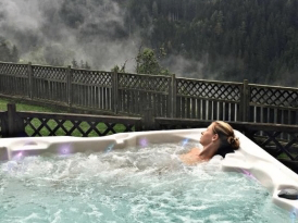Eine Frau entspannt sich in einem Whirlpool mit Blick auf eine neblige Berglandschaft und einen Holzzaun im Hintergrund.