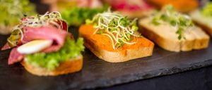 Eine Auswahl an Gourmet-Sandwiches mit einzigartigen Belägen ist auf einem Schieferbrett ausgestellt. Die Sandwiches enthalten Sprossen und verschiedene Aufstriche und präsentieren eine Vielfalt an Aromen und Texturen.