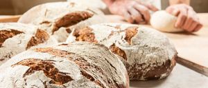 Nahaufnahme mehrerer frisch gebackener Brotlaibe mit einer Hand im Hintergrund.