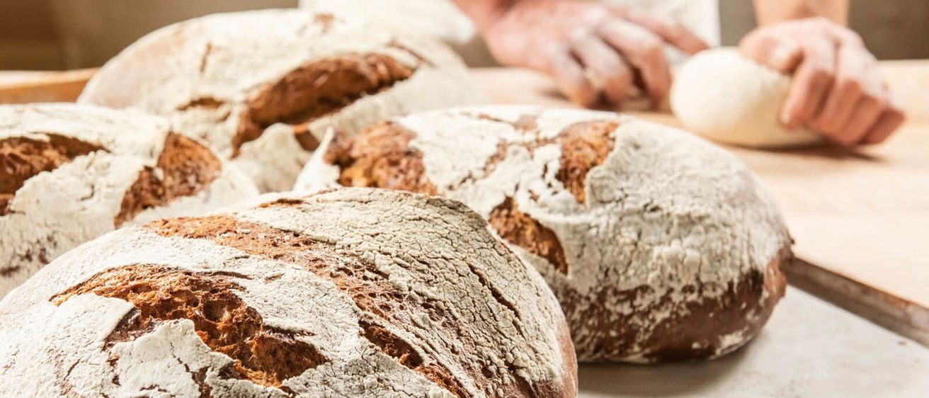 Nahaufnahme mehrerer frisch gebackener Brotlaibe mit einer Hand im Hintergrund.