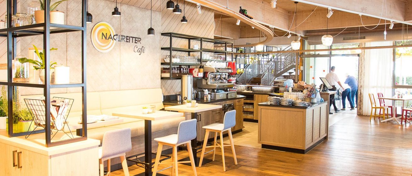 Das Interieur von Naclreiter Cafe hat Holzböden, weiße Wände und moderne Möbel. Es hat eine Kaffeemaschine und einen Regal mit ausgestellten Artikeln.