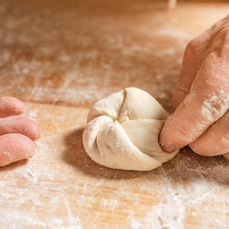 Eine Person formt Teig zu einem Knoten auf einer bemehlten Oberfläche, wobei ihre Hände mit Mehl bedeckt sind.