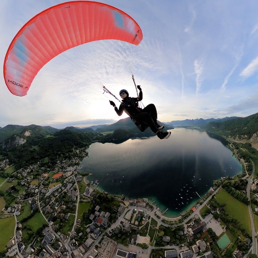 Eine Person paragliding über einem See mit Bergen im Hintergrund und einer kleinen Stadt darunter.