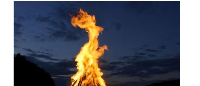 Ein Lagerfeuer brennt nachts auf einem Hügel. Die Veranstaltung heißt 'Einladung zur Sonnwendfeier.' Der Ort ist im Zentrum von Jagerberg.