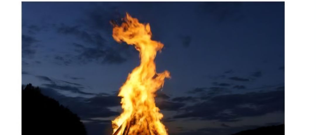 Ein Lagerfeuer brennt nachts auf einem Hügel. Die Veranstaltung heißt 'Einladung zur Sonnwendfeier.' Der Ort ist im Zentrum von Jagerberg.
