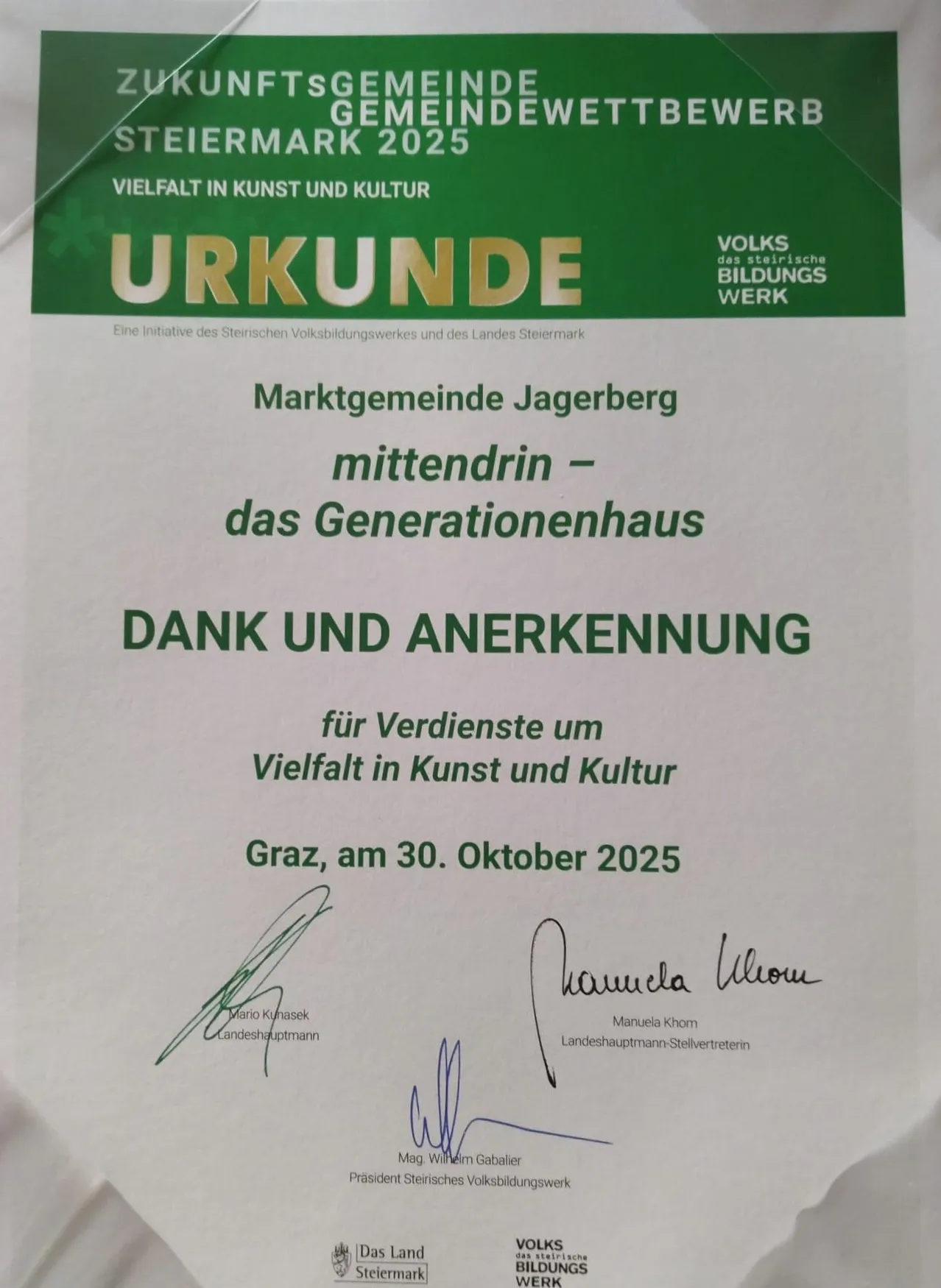 Ein Zertifikat mit dem Titel 'Urkunde' vom Volksbildungswerk würdigt die Marktgemeinde Jagerberg für Verdienste in Kunst und Kultur, datiert auf den 30. Oktober 2025. Unterzeichnet von Mario Kunasek und Manuela Khom.