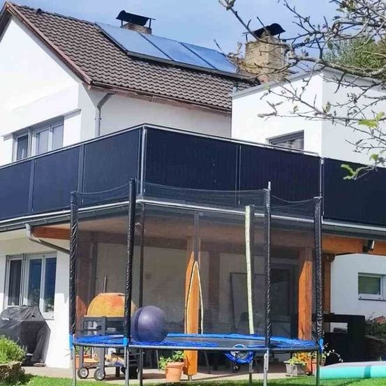 Ein modernes Haus mit solarbetriebenem Dach, Balkon und eingezäuntem Trampolin im Garten.