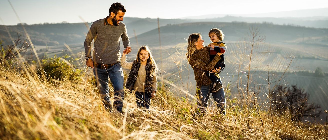 Eine Familie mit zwei Kindern geht auf einem Hügel, mit einer schönen Landschaft im Hintergrund.