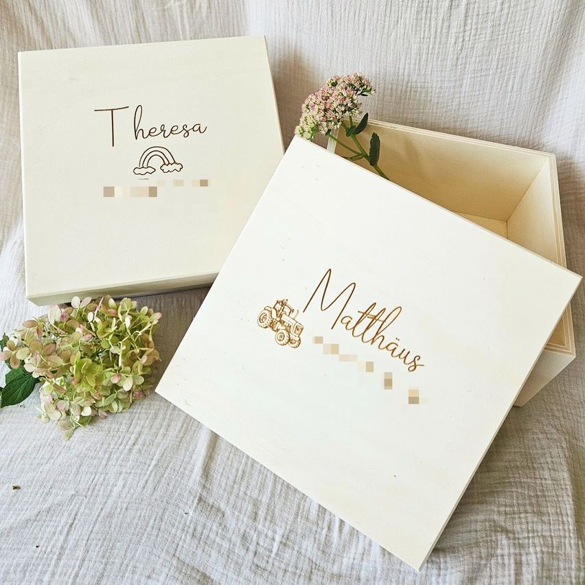Two personalized boxes labeled Theresa and Matthias sit on a cloth with flowers. Theresa has a rainbow, Matthias has a tractor.