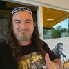 Ein Mann mit einer Sonnenbrille auf dem Kopf lächelt vor einem Café-Banner mit einem Mann, der singt.