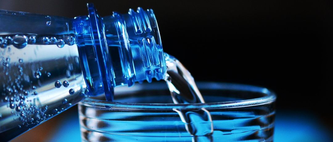 Eine blaue Flasche gießt Wasser in ein Glas und hält den Moment des Wasserstrahls fest.