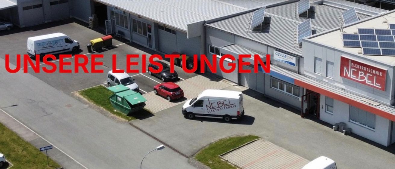 Eine Luftaufnahme eines Gebäudes mit Solarmodulen auf dem Dach. Ein weißer Lieferwagen ist davor geparkt. Das Gebäude hat ein Schild mit der Aufschrift NGEN links und Elektrotechnik Nebel rechts.