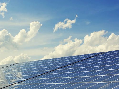 Ein Solarpanel ist unter einem blauen Himmel mit verstreuten Wolken installiert. Die Sonnenstrahlen reflektieren auf dem Panel.