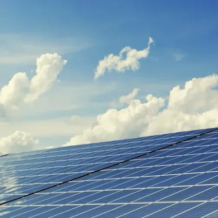 Ein Solarpanel-Array ist unter einem teilweise bewölkten blauen Himmel positioniert und reflektiert Sonnenlicht.