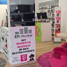 Ein Innenaufnahme eines Geschäftsbetriebs mit einem Banner, das Magenta Business in der Mitte bewirbt und einen Mann auf der rechten Seite zeigt.