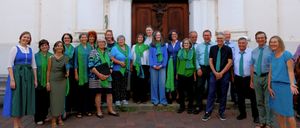 Eine Gruppe von Menschen, die grüne und blaue Schals tragen, steht vor einem Gebäude. Sie lächeln und posieren für ein Foto.