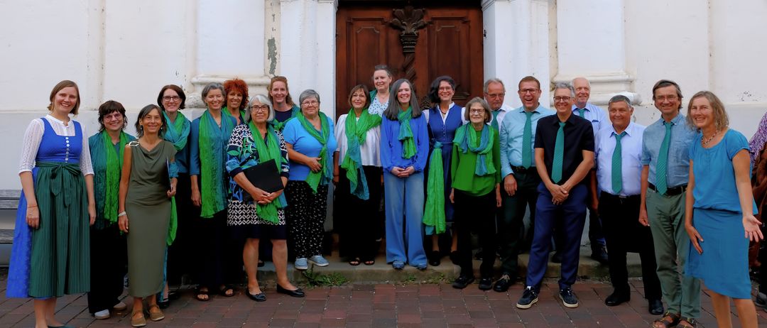 Eine Gruppe von Menschen, die grüne und blaue Schals tragen, steht vor einem Gebäude. Sie lächeln und posieren für ein Foto.