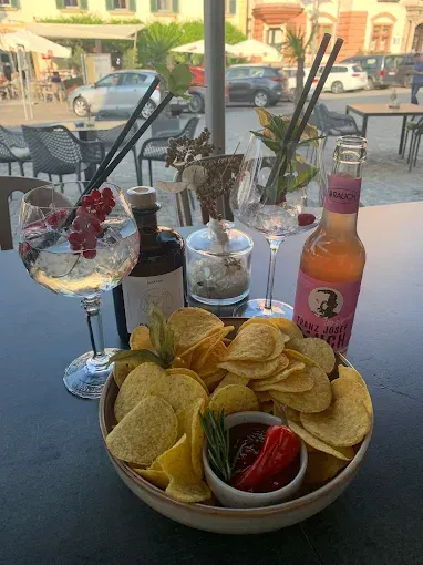 Ein Tisch mit einer Schüssel Pommes, Getränkeflaschen und Gläsern ist im Freien aufgestellt.