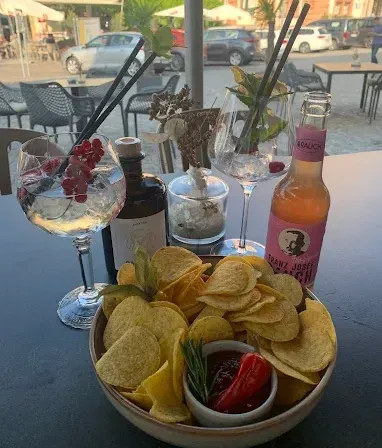 Ein Tisch mit einer Schüssel Pommes, Getränkeflaschen und Gläsern ist im Freien aufgestellt.