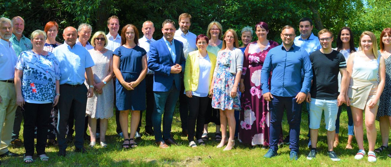 Eine Gruppe von Menschen steht in einem Park, umgeben von Bäumen. Sie sind lässig gekleidet und posieren wahrscheinlich für ein Gruppenfoto.