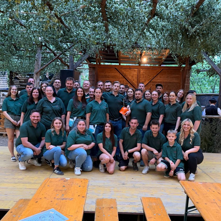 Gruppe von Mitarbeitern in grünen Poloshirts posiert vor Holzhütte in Österreich