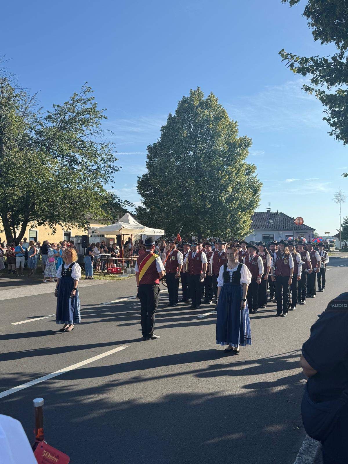 Eine Musikkapelle in traditioneller Kleidung tritt auf der Straße auf, während eine Menschenmenge zuschaut.