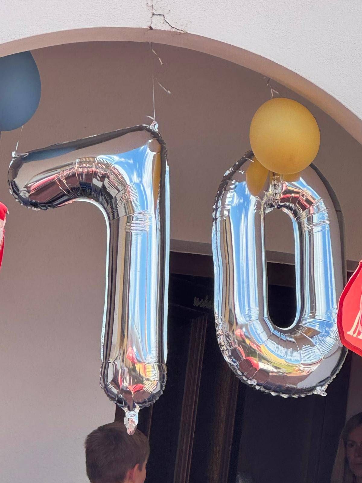 Silberne Folienballons bilden die Zahl 70 und hängen von der Decke, mit einem gelben Ballon im Hintergrund.