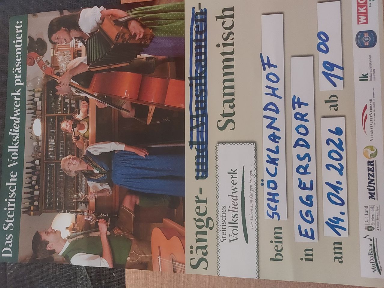 Ein Poster zeigt eine Gruppe von Musikern, die Instrumente wie Cello und Gitarre spielen. Der Text ist auf Deutsch und enthält Wörter wie Stammtisch, Schocklandhof und Eggersdorf.
